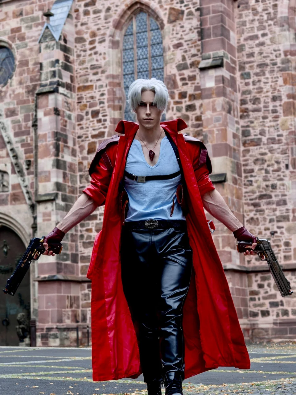 Dante cosplay from Devil May Cry walking forward with two pistol props in front of gothic architecture.