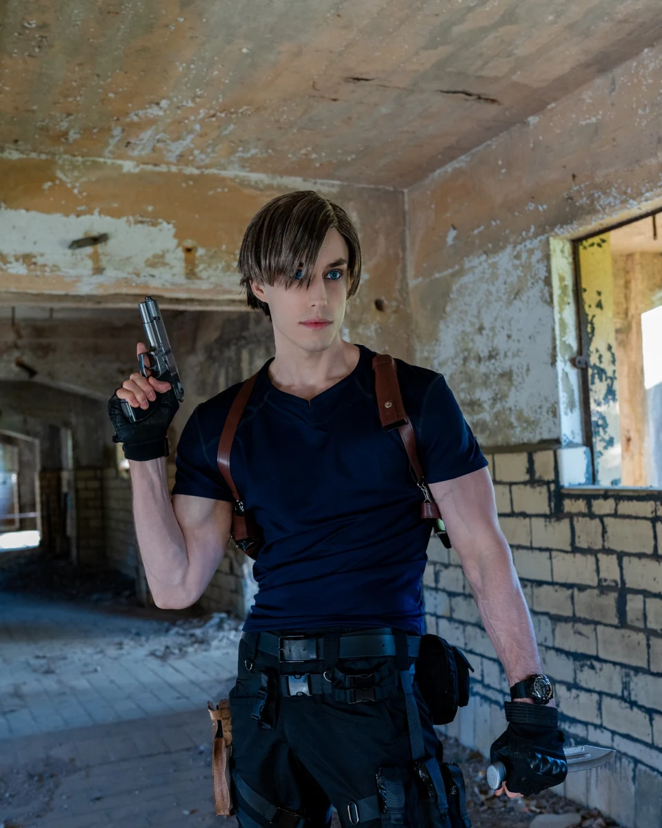 Leon S. Kennedy cosplay portrait in a dark tactical outfit with shoulder holster and handgun prop inside an abandoned industrial building.