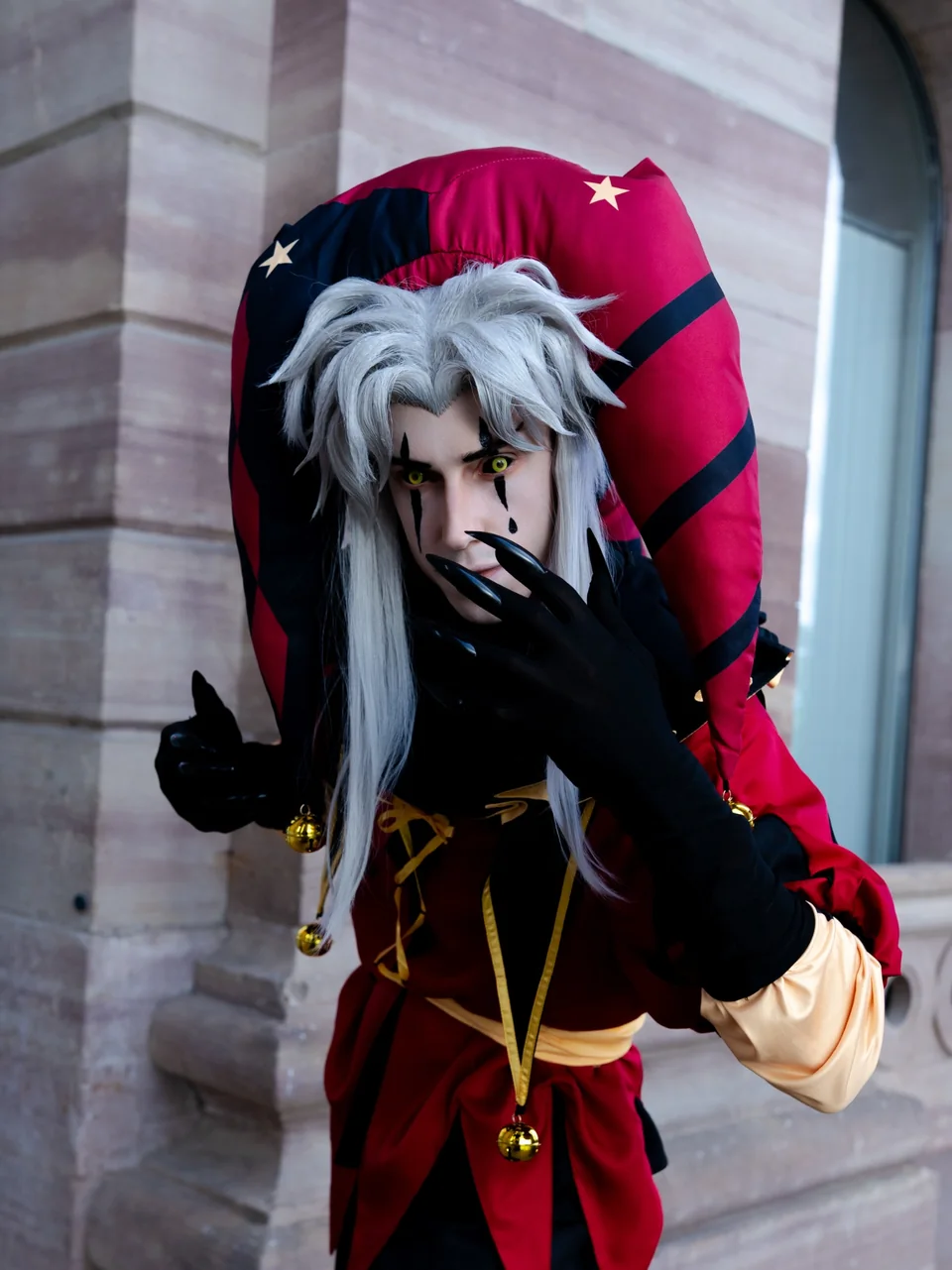 Jester-inspired cosplay portrait with white hair, dramatic makeup and red-black costume.