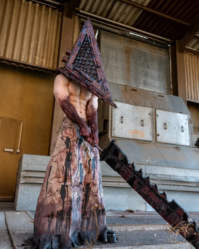 Horror cosplay with a large handcrafted pyramid helmet and oversized prop weapon.