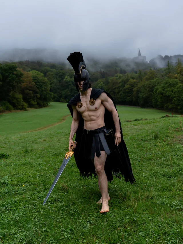 Full-body Agamemnon cosplay holding a sword in a fog-covered landscape.