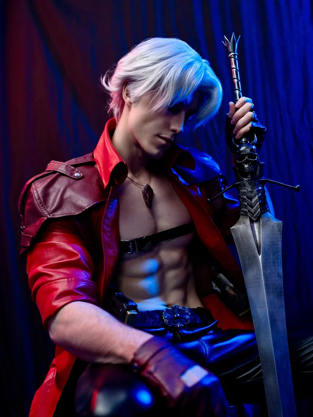 Studio portrait of Dante cosplay from Devil May Cry seated beside the 3D-printed sword under red and blue lighting.