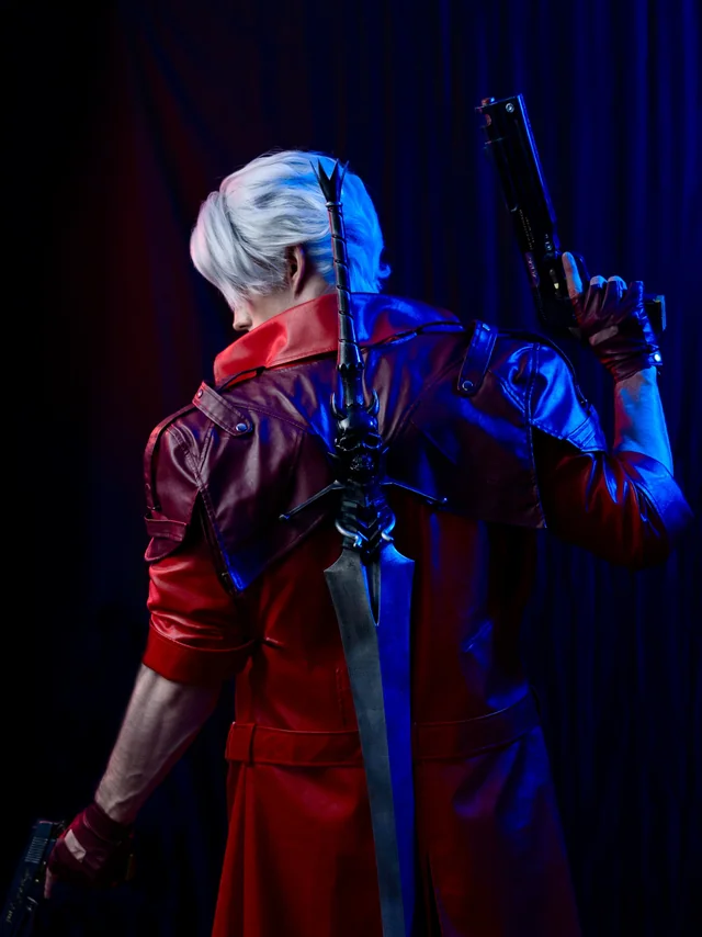 Rear studio view of the Dante cosplay showing the red coat, 3D-printed sword, shoulder details and pistol prop under red and blue lighting.