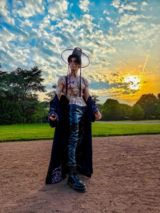Full-body Jinu cosplay at sunset with purple body markings, black outfit and a wide traditional hat.