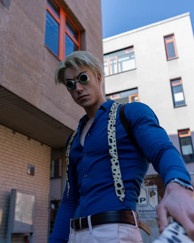 Kento Nanami cosplay in a blue shirt, patterned tie and round goggles photographed outdoors.