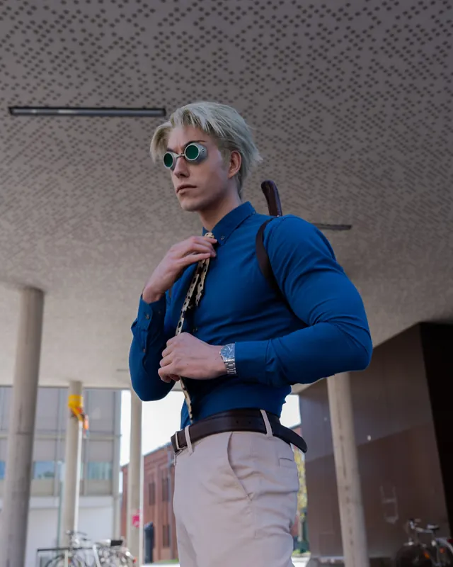 Kento Nanami cosplay in a blue shirt and round goggles while adjusting a patterned tie.