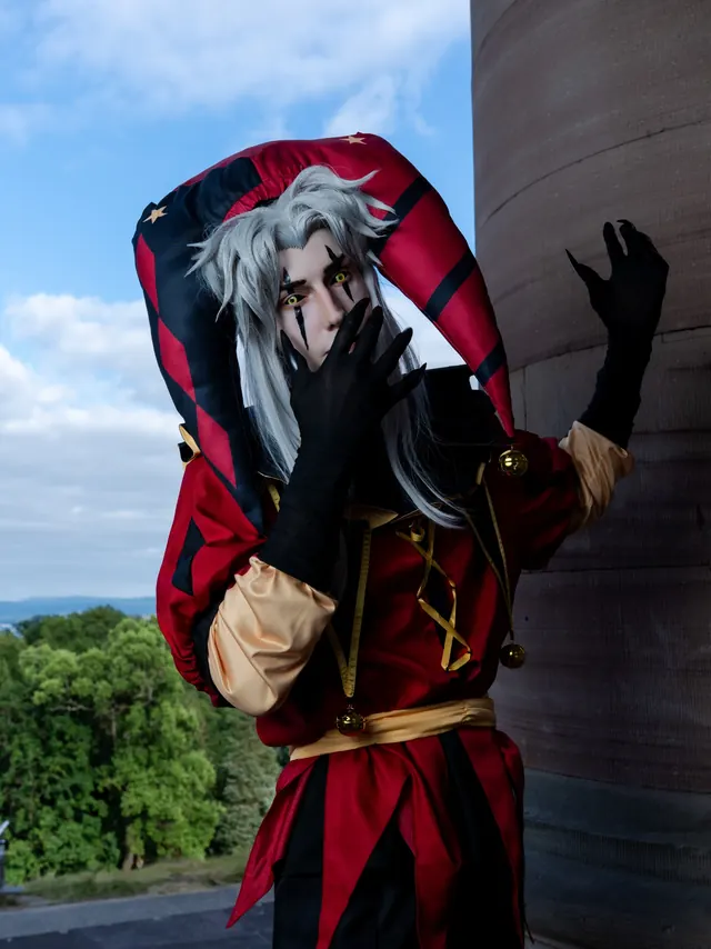Pierrot cosplay portrait in a red and black jester costume with white hair and dramatic makeup.