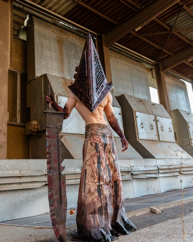 Full-body Pyramid Head cosplay in an industrial setting with a handcrafted helmet and oversized blade.