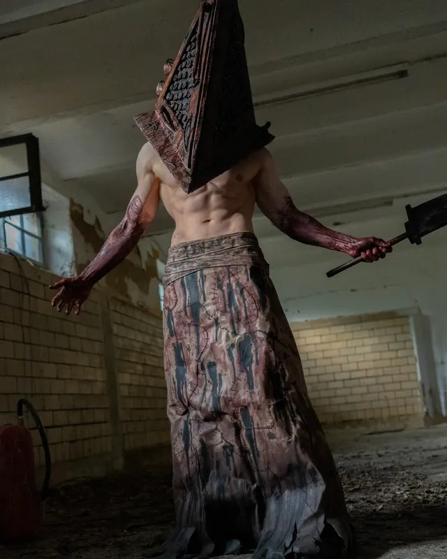 Pyramid Head cosplay in a dark abandoned interior with a handcrafted helmet and heavy weapon.