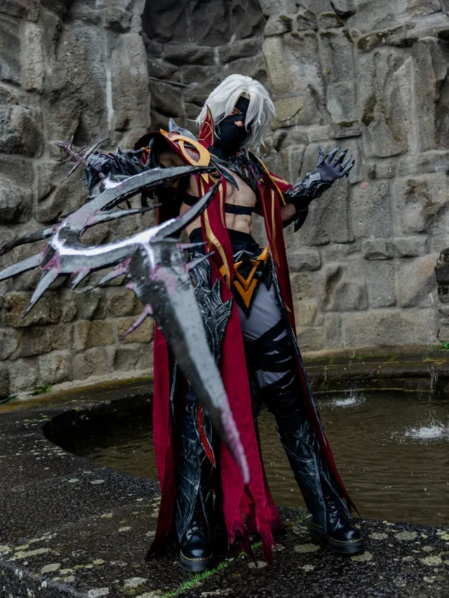 Full-body Rerir cosplay in a stone courtyard with black and red armor and a large fantasy blade.