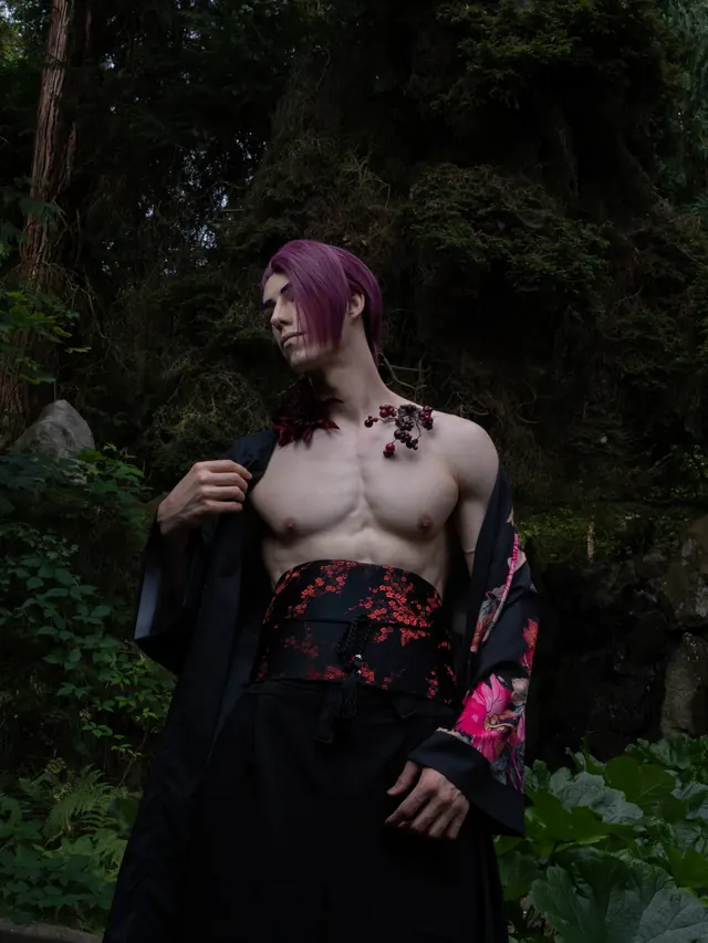 Rien cosplay with purple hair and a dark floral robe photographed among dense greenery.