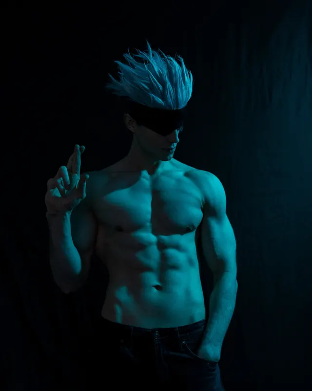 Satoru Gojo cosplay in blue studio light with white hair, blindfold and a hand-sign pose.