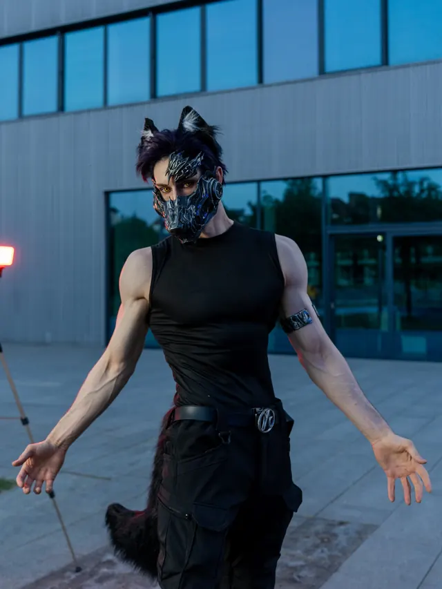 Valko cosplay standing in a black sleeveless outfit with a metallic creature mask and black ears.