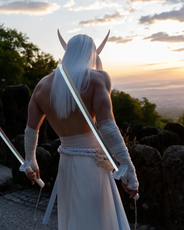 Rear-view Yone cosplay at sunset with long white hair and two glowing sword props.